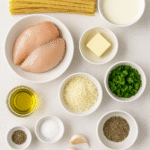 Ingredients for Chicken Alfredo Pasta including fettuccine, chicken breast, garlic, butter, cream, parmesan, and parsley arranged on a kitchen counter.