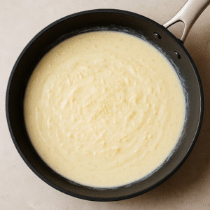 Creamy Alfredo sauce simmering in a skillet with butter, garlic, heavy cream, and parmesan for Chicken Alfredo Pasta.