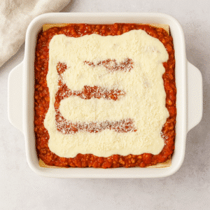 Baking dish with layers of lasagna pasta sheets, ragù sauce, creamy béchamel, and parmesan cheese before baking.
