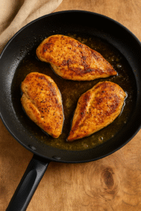 Chicken breasts cooking in a non-stick skillet with melted butter and olive oil until golden brown.
