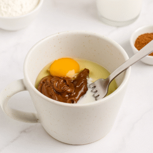 Mixing wet ingredients like Nutella, milk, egg, and oil in a mug to prepare the nutella mug cake batter.