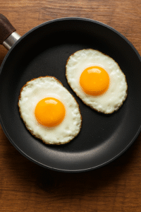 Sunny side up eggs cooking in a non-stick pan for avocado egg toast.