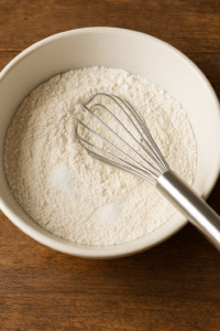 Mixing dry ingredients for fluffy pancakes in a bowl with a whisk.