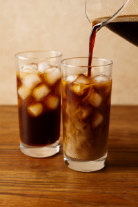 Pouring cold brewed coffee over ice cubes to prepare iced coffee.