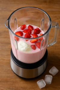 Adding strawberries, yogurt, and milk into a blender to make a strawberry smoothie.