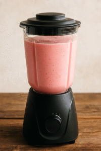 Blending a creamy pink strawberry smoothie in a blender.