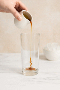 Pouring caramel syrup into a tall glass for homemade iced caramel latte.