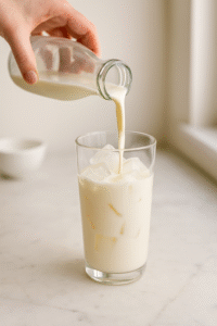 Pouring cold milk into a tall glass filled with ice cubes for iced caramel latte.