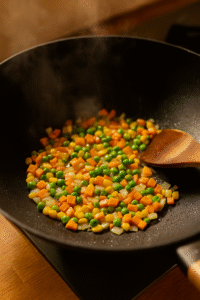 Soft scrambled eggs cooking in sesame oil inside a wok as the first step for Vegetable Fried Rice, with steam rising and golden texture visible.