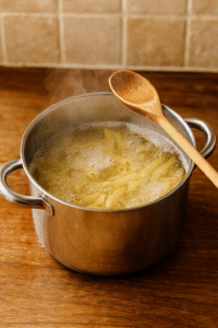 Pasta boiling in salted water with steam rising, the first step in making Creamy Pesto Chicken Pasta.