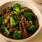 Beef and broccoli stir fry served in a bowl with sesame seeds and green onions on top. 🌿🍚
