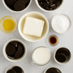 No-Bake Oreo Cheesecake ingredients – Oreo cookies, cream cheese, heavy cream, powdered sugar, vanilla, and melted butter on table.