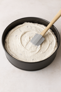 No-Bake Oreo Cheesecake step 3 – creamy Oreo filling poured over crust and smoothed with spatula in springform pan.