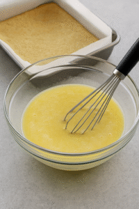 Lemon Bars step 2 – lemon filling mixture of eggs, sugar, flour, and lemon juice being whisked in glass bowl