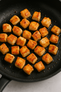 Golden seared chicken cubes in a pan for creamy garlic parmesan chicken bites
