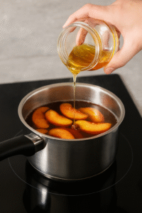 Pouring honey into a saucepan with peaches and tea while making peach iced tea.