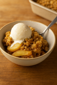 Warm apple crumble served in a bowl with vanilla ice cream on top.