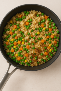 Cooked rice mixed with peas, carrots, and corn inside a skillet, seasoned with soy sauce — Garlic Butter Steak Fried Rice base.