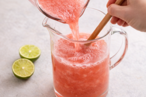 Adding cold water and fresh lime juice to watermelon agua fresca in a pitcher