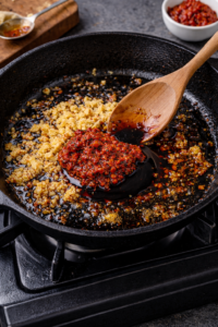Garlic and ginger sautéed with chili paste and soy sauce in a skillet.
