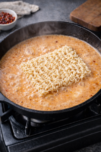 Ramen noodles cooking directly in creamy spicy chicken broth.