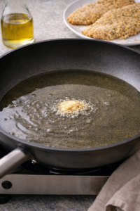 Heating oil in a skillet until sizzling hot for frying crispy Parmesan chicken cutlets.