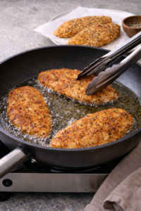 Frying crispy Parmesan chicken cutlets until golden brown and crunchy in hot oil.