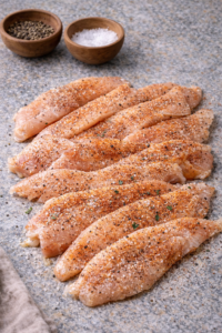 Seasoned chicken strips ready to cook for a crispy chicken caesar salad wrap.