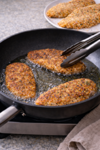 Pan-frying breaded chicken until golden for a crispy chicken caesar salad wrap.