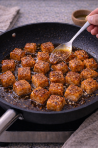 Glazing honey garlic salmon bites with sticky honey garlic sauce in a skillet.