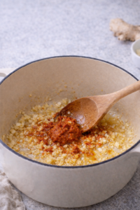 Garlic and ginger sautéed with red curry paste in a pot.