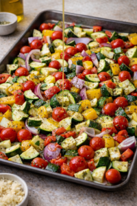 Fresh zucchini, bell peppers, onion, and cherry tomatoes tossed with olive oil and herbs on a baking sheet