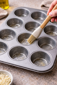 Greased metal muffin tin prepared for baking savory breakfast muffins
