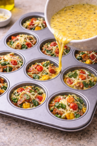 Egg mixture poured over vegetable and cheese filling in muffin tin