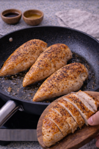 Searing seasoned chicken in a skillet until golden for creamy sesame chicken ramen.