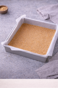 Baked graham cracker crust cooling in pan for strawberry cheesecake bars.