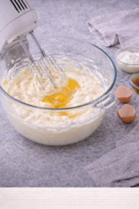 Mixing creamy cheesecake filling with cream cheese and eggs for strawberry cheesecake bars.