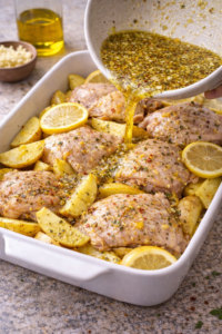 Chicken thighs and potato wedges in a baking dish with lemon garlic marinade poured over