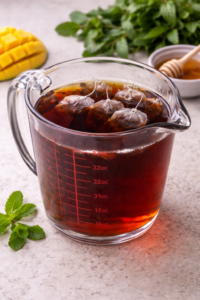 Black tea bags steeping in hot water in a glass pitcher for mango iced tea