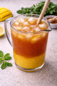 Mango iced tea with ice cubes stirred in a glass pitcher until cold